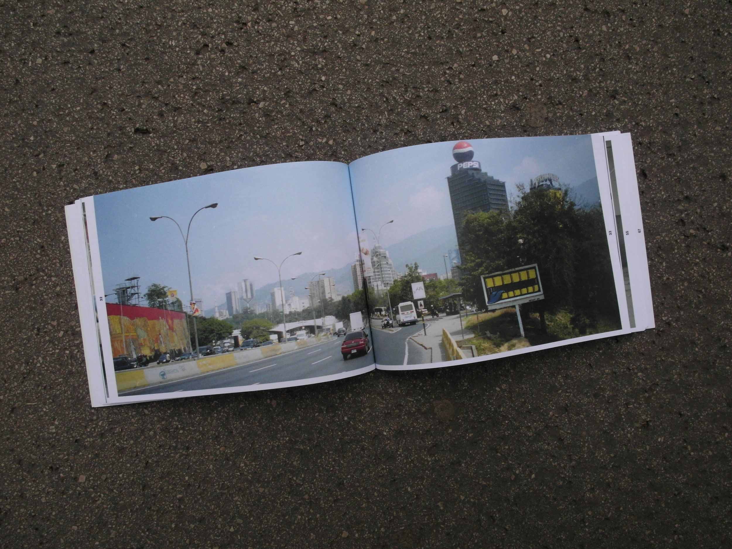 Open book lying on the street. Photo of city highway in southamerican city over entire double page. Motif painted in yellow/black on old advertising sign.